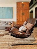 Leather-covered armchair and cushions in front of simple, Oriental-style wooden cupboard