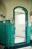 Bathroom with turquoise wall tiles and rounded archway leading to shower