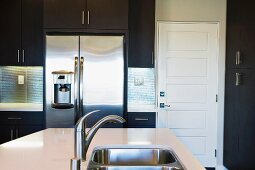 Unterbauspülbecken in modernem Küchenblock und Edelstahlkühlschrank im Hintergrund