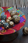 Wooden balls with carved patterns in wooden dish covered in colourful fabric scraps