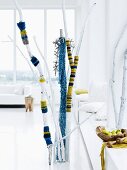 Branches covered with blue and yellow striped, knitted textiles as decoration in reserved, white interior