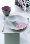 Japanese place setting on white side table with decorative bowl of twigs and blossom in background