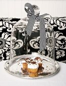 Cupcakes topped with whipped cream and grated chocolate under a glass cloche