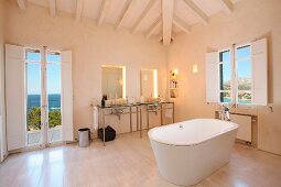 Freistehende Badewanne unter Holzbalkenedecke im minimalistischen Bad mit Meerblick