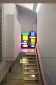 View of floating staircase treads and shelves of multi-coloured light boxes in designer apartment through glass balustrade