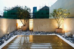 Wooden roof terrace wet with rain in front of illuminated potted plants on strips of gravel