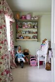 Blick durch offene Kinderzimmertür auf Puppen in Kinderbuggy, Wandregal mit Spielzeug und Schabrackenvorhang mit Rosenmuster wirkt nostalgisch