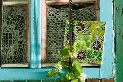 Small mirror with broad floral frame and brightly painted window frame with crochet curtains