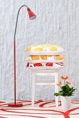 Scatter cushions on stool next to red standard lamp on red and white patterned rug