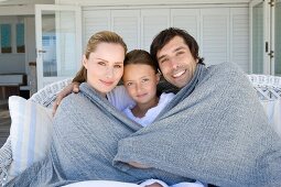 Familie mit einem Kind sitzt mit Decke auf der Terrasse