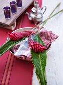 Place setting with tropical flowers on patterned linen napkin; Moroccan silver teapot and tea glasses in background