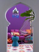 Blick durch Schlüssellochfenster auf orientalisch inspirierten Wohnraum mit blauem Korbtisch und Matrazensofa