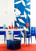 Dining table, stool, plastic chairs & photographic wallpaper in interior in shades of blue & red