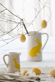 Branches with Easter eggs in white pitchers decorated with bunny rabbits