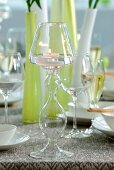 Lit tealight in glass candlestick in front of vases and wine glasses on table