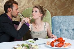 Paar in Abendkleidung trinkt Sekt zu Hummer und Austern