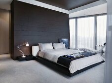 Breakfast tray on a double bed in front of a black tiled room partition in a minimalist bedroom