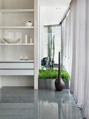 White bookshelves serving as a room partition next to floor vase and plant pot on a high gloss stone floor