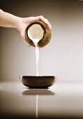 Hand Pouring Milk Out of a Coconut into a Bowl