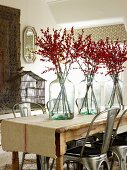 Branches of berries in glass vases on table and retro metal chairs in simple interior