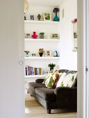 View into a living room - brown sofa with colorful pillows and shelves built into a wall niche