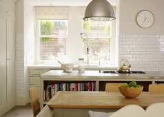 Country-house charm- simple dining table in front of kitchen island with hob and counter with sink below window