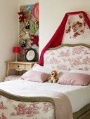 Traditional double bed with upholstered headboard and foot next to bedside table in niche below soft toys on pinboard