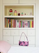 Bed in front of fitted cabinet with shelves and handbag hanging from drawer handle