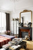 Bedroom with an antique coffee table on wheels next to a bed, fireplace and gold framed mirror