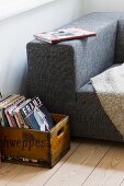 Vintage wooden crate of books next to partially visible modern couch with mottled grey fabric cover