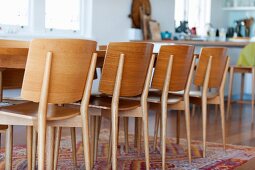 Simple, modern wooden chairs around dining table on colourful rug