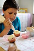 Kleiner Junge verziert Cupcakes mit Creme