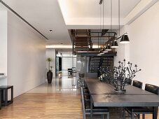 Esstisch aus dunklem Holz in offenem Wohnraum mit wechselndem Bodenbelag und Blick auf Treppe