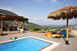 Ruheliegen mit bunten Badetüchern und Sonnenschirm am Swimmingpool auf der Terrasse (Villa Octavius, Lefkas, Griechenland)