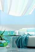 In Aquafarben gestalteter Wohnbereich mit Sofa und Beistelltisch unter gestreiftem Sonnensegel