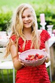 A blonde girl with a bowl of freshly picked strawberries