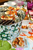 Prawn kebabs with crispy bacon pieces on a tabletop barbecue at a buffet