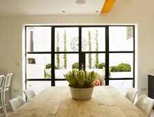 Bowl of hyacinths on rustic wooden table in front of window with black lattice and view of modern courtyard