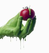 A green-painted hand holding a tomato