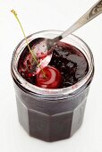 A jar of cherry jam with a fresh cherry and a spoon