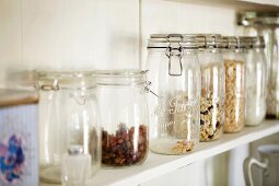 Various dried fruits and cereals in storage jars on a kitchen shelf