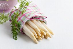 Geschälter weisser Spargel im Küchentuch mit Karottengrün