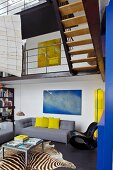 Modernes, poppiges Wohnzimmer mit grauem Designersofa unter der Galerie und auffälligem Zebrateppich
