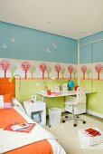 Pastellfarben im Kinderzimmer - in Schablonentechnik bemalte Wand hinter neutral weißem Schreibplatz und orangefarben bezogenem Bett
