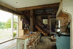 Open-plan, country-house-style living-dining room with rustic wooden floor and wooden staircase leading to mezzanine; open terrace window leading to garden