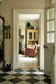 Open front door in hallway with chequered tiles on floor and view into comfortable living room with vintage-style white floorboards and dresser