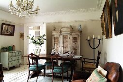 Living-dining room with crystal chandelier, antique dining table and elegant upholstered chairs on rustic, white-painted wooden floor and shabby-chic furniture