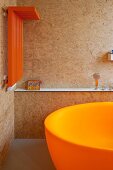 Corner of a bathroom with an orange, heated towel rail on a wall made of particle board and a partially visible bath tub