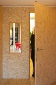 Open door in room clad with chipboard made of large wood chips