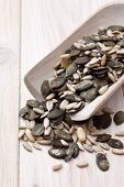 Sunflower seeds, pumpkin seeds and pine nuts on a wooden scoop (close-up)